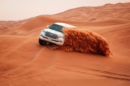 A mechanic inspecting the tires and suspension of a 4x4 SUV before a desert safari, ensuring adherence to Dune bashing safety tips Saudi Arabia and vehicle maintenance standards.