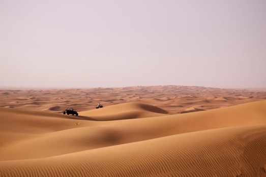 Tourists experiencing the thrill of sandboarding and dune bashing on golden sand dunes under a bright sky, highlighting the adventure awaiting travelers on Half Day Desert Tours in Jeddah.