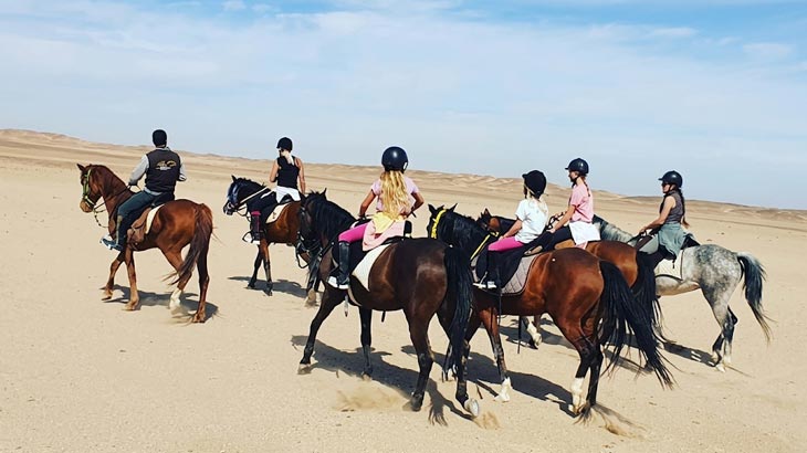 Guided group horse riding tour riding in formation through the Jeddah desert dunes.