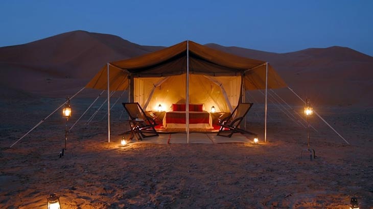 Luxury desert glamping tent rental illuminated at night in the Jeddah desert sand dunes.
