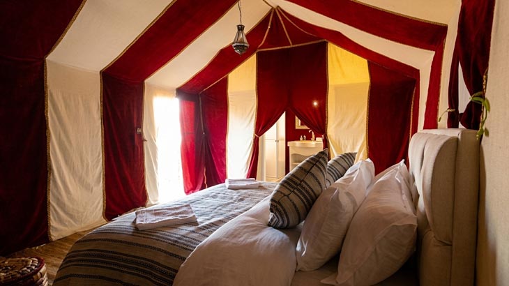 Interior view of a luxury desert glamping tent bedroom rental in Jeddah with red and white fabric draping.